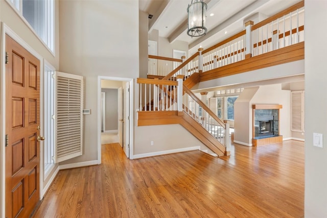 foyer with stairway, a high ceiling, wood finished floors, a tile fireplace, and baseboards