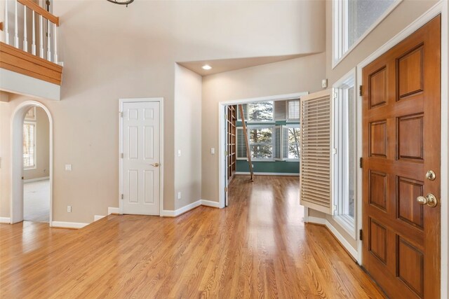 foyer featuring arched walkways, baseboards, a towering ceiling, and light wood finished floors