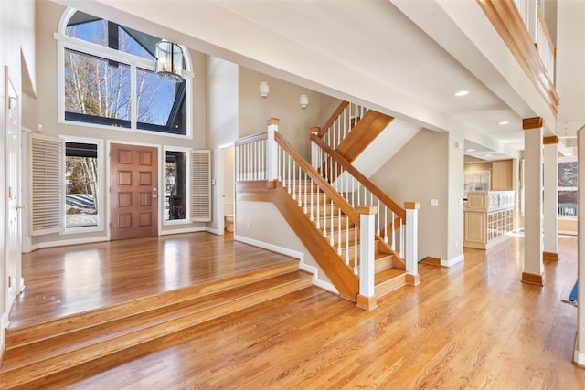 foyer entrance featuring light wood-style floors, a towering ceiling, baseboards, and stairs