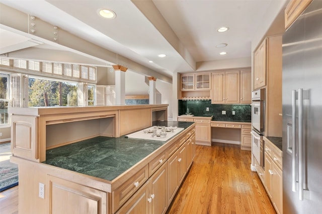 kitchen featuring light brown cabinets, white appliances, light wood finished floors, glass insert cabinets, and tasteful backsplash