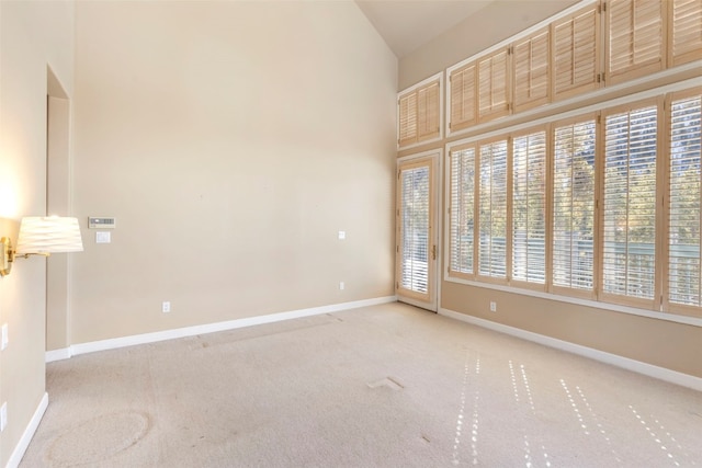 carpeted empty room with a towering ceiling and baseboards