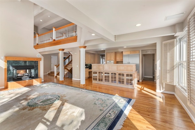 living area with light wood-style floors, a high end fireplace, beamed ceiling, baseboards, and stairs