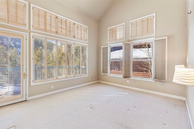 carpeted empty room with high vaulted ceiling and baseboards