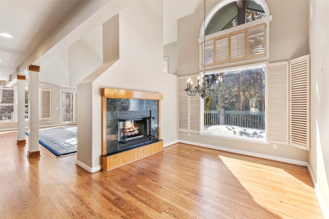 unfurnished living room featuring a fireplace, wood finished floors, a towering ceiling, and baseboards