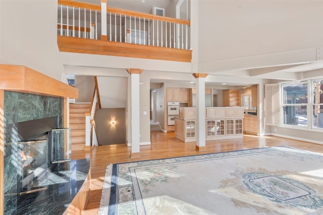 unfurnished living room featuring a tile fireplace, a towering ceiling, baseboards, stairway, and light wood finished floors