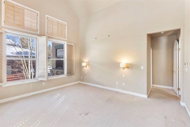 carpeted spare room featuring high vaulted ceiling and baseboards