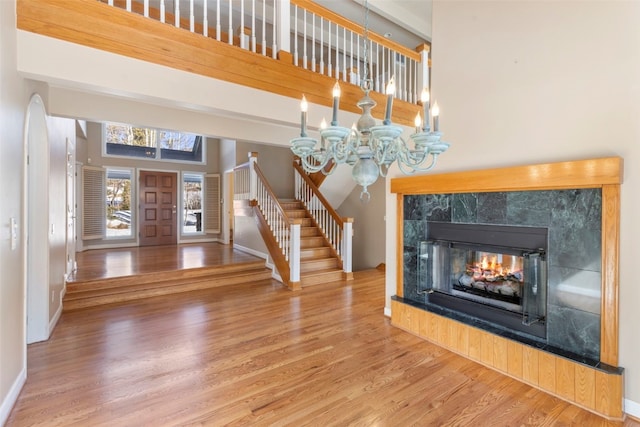 foyer with a tile fireplace, a notable chandelier, wood finished floors, baseboards, and stairway