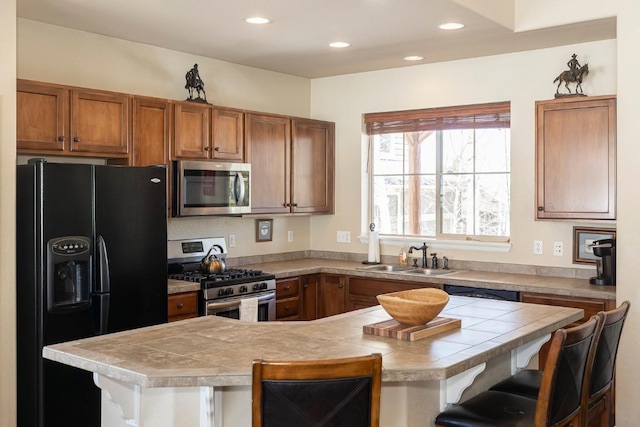 kitchen featuring brown cabinetry, a kitchen breakfast bar, a sink, and appliances with stainless steel finishes