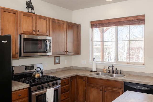kitchen with black appliances, brown cabinets, a sink, and light countertops