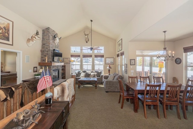 dining area with carpet floors, high vaulted ceiling, a stone fireplace, and ceiling fan with notable chandelier