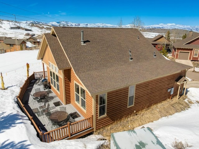 snow covered back of property with roof with shingles and a deck with mountain view