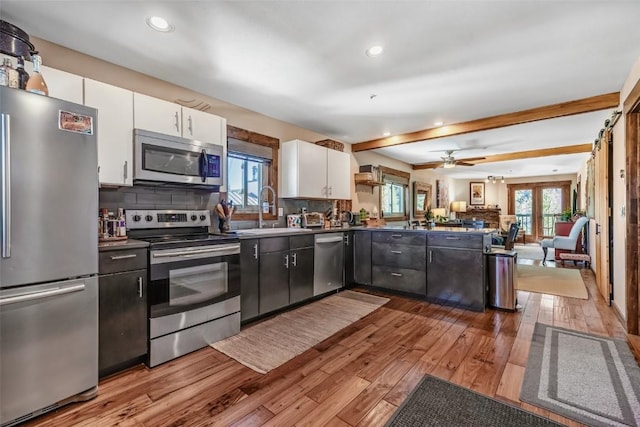 kitchen featuring white cabinets, stainless steel appliances, a peninsula, open floor plan, and wood-type flooring