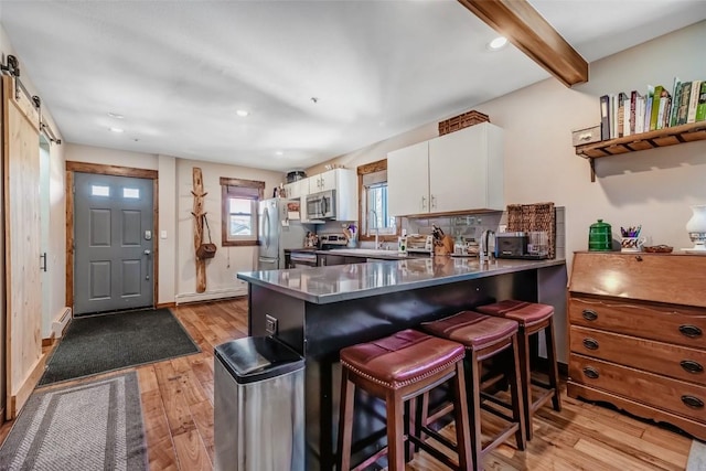 kitchen with a peninsula, light wood-style flooring, a kitchen bar, white cabinetry, and appliances with stainless steel finishes