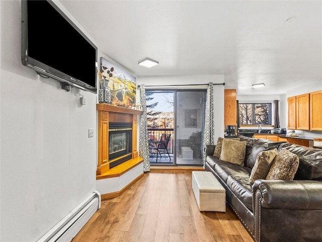 living area featuring light wood-type flooring, plenty of natural light, a glass covered fireplace, and a baseboard radiator