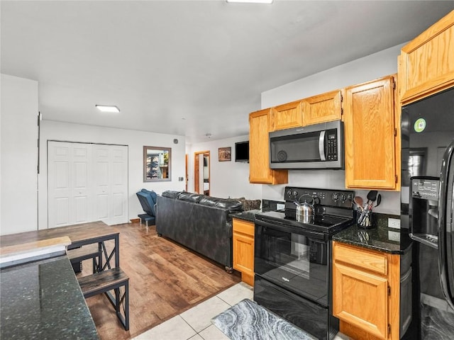 kitchen featuring dark stone countertops, tile patterned flooring, open floor plan, and black appliances