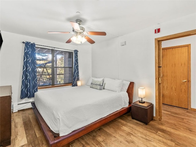 bedroom with baseboards, a ceiling fan, wood finished floors, and a baseboard radiator