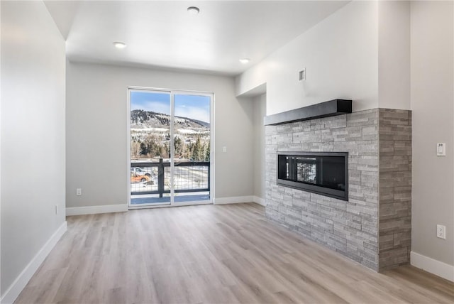 unfurnished living room with a mountain view, a stone fireplace, and light hardwood / wood-style flooring