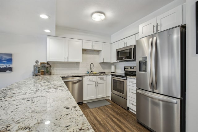 kitchen featuring stainless steel appliances, white cabinetry, decorative backsplash, light stone countertops, and dark wood-type flooring