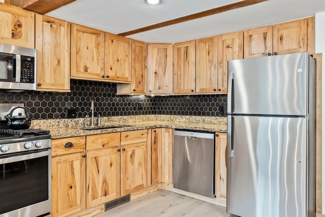 kitchen with visible vents, light stone countertops, tasteful backsplash, a sink, and stainless steel appliances