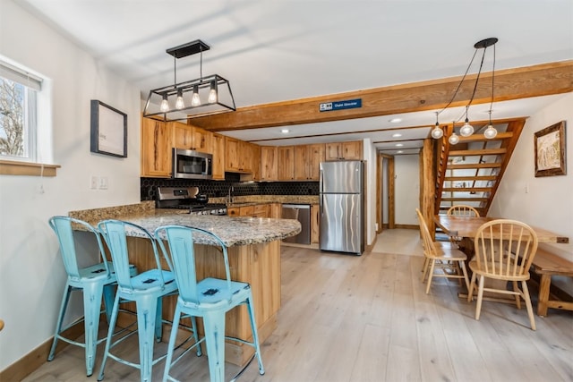 kitchen with light stone countertops, brown cabinetry, stainless steel appliances, a peninsula, and tasteful backsplash