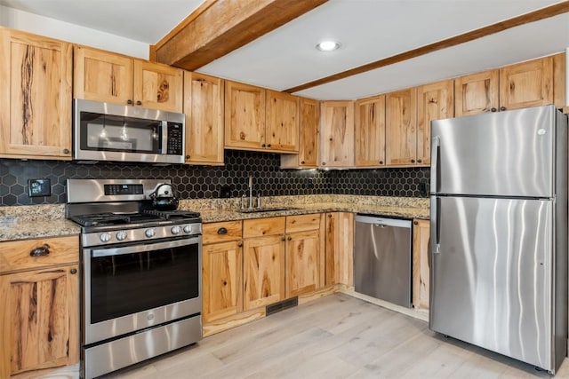 kitchen featuring stainless steel appliances, light stone countertops, a sink, and light wood-style flooring