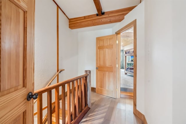 hallway with baseboards, light wood-style flooring, beam ceiling, and an upstairs landing