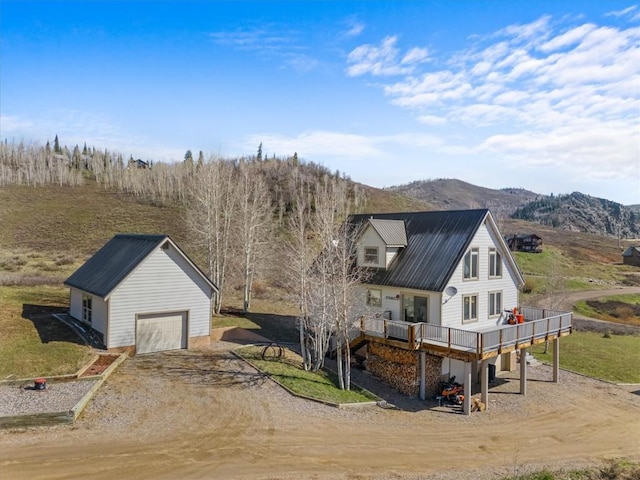57680 Saturn Ct, Clark, CO 80428 - view of front of house featuring an outdoor structure, a deck with mountain view, a detached garage, dirt driveway, and metal roof