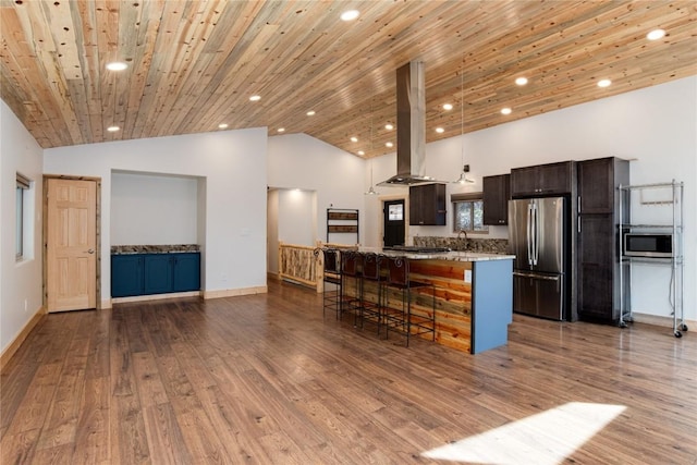 kitchen with dark brown cabinets, wood finished floors, island range hood, appliances with stainless steel finishes, and a breakfast bar area
