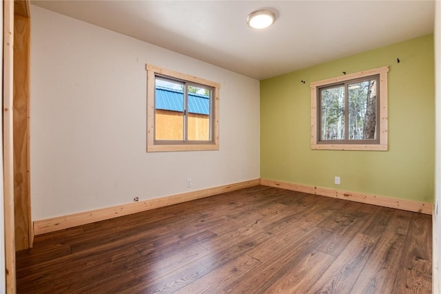 spare room featuring baseboards, wood finished floors, and a wealth of natural light