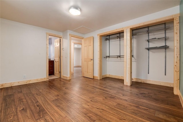 unfurnished bedroom with two closets, baseboards, and wood finished floors