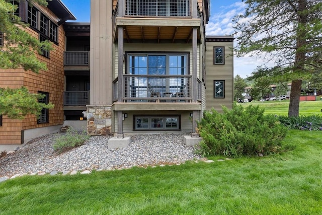 back of house featuring a yard, stone siding, and a balcony