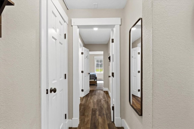 hall featuring baseboards, a textured wall, and dark wood-style floors