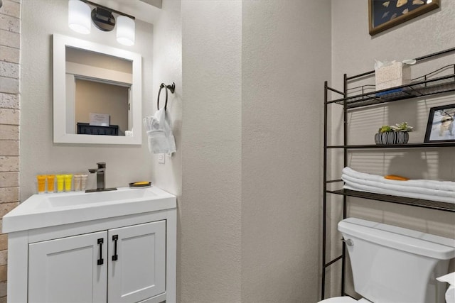 half bathroom with toilet, a textured wall, and vanity
