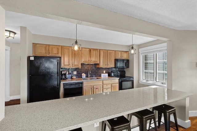 kitchen featuring a kitchen breakfast bar, a sink, baseboards, backsplash, and black appliances