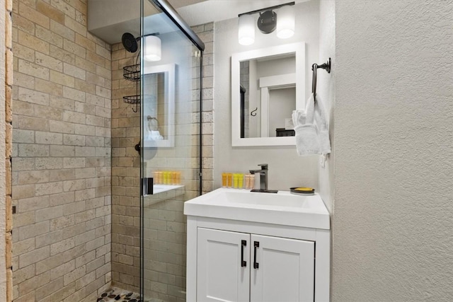 full bathroom with a shower stall, a textured wall, and vanity