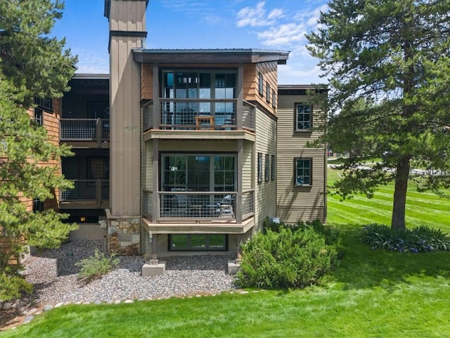 rear view of property featuring stone siding, a lawn, and a balcony
