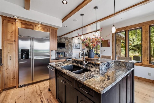 240 Two Cabins Dr, Silverthorne, CO 80498 - kitchen featuring stainless steel appliances, beamed ceiling, light wood-style floors, a kitchen island with sink, and dark stone countertops