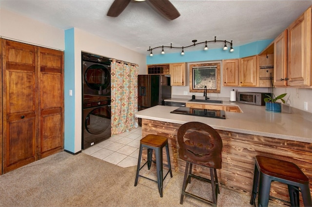 kitchen featuring a peninsula, a sink, a breakfast bar, stacked washing maching and dryer, and black appliances