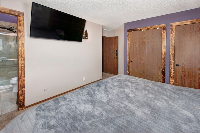 bedroom with a textured ceiling, baseboards, two closets, ensuite bath, and carpet floors