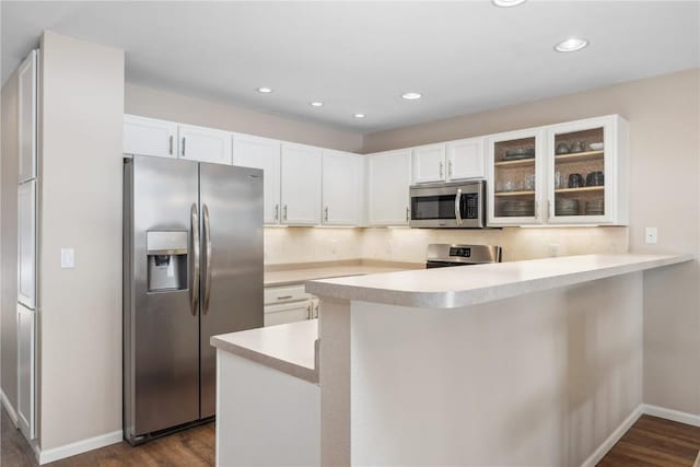 kitchen featuring dark wood finished floors, a peninsula, stainless steel appliances, and glass insert cabinets