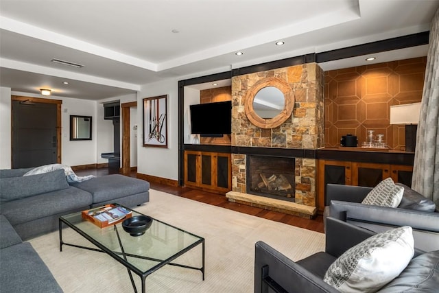 living area with visible vents, baseboards, wood finished floors, and a tray ceiling