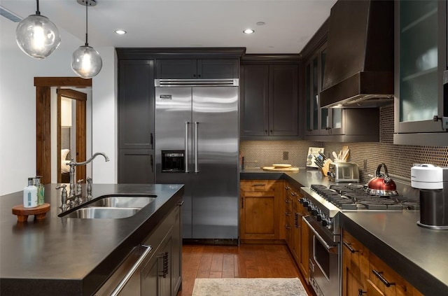 kitchen with wall chimney range hood, hardwood / wood-style floors, premium appliances, a sink, and backsplash
