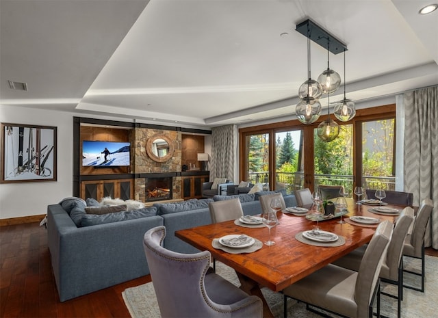 dining area featuring a stone fireplace, hardwood / wood-style floors, a tray ceiling, baseboards, and visible vents