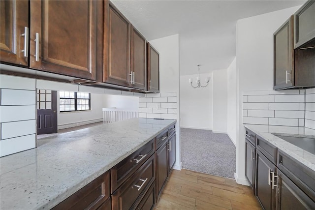 kitchen featuring baseboards, light stone counters, tasteful backsplash, and a chandelier