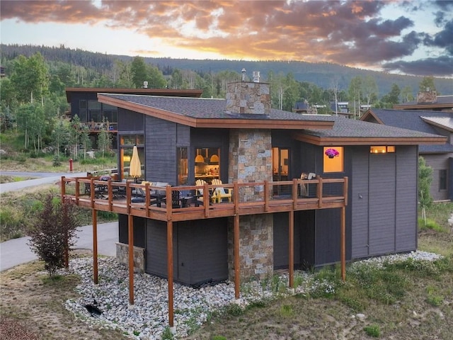 22 Vernon Way, Silverthorne, CO 80498 - back of house at dusk featuring stone siding, a deck with mountain view, a chimney, and a shingled roof