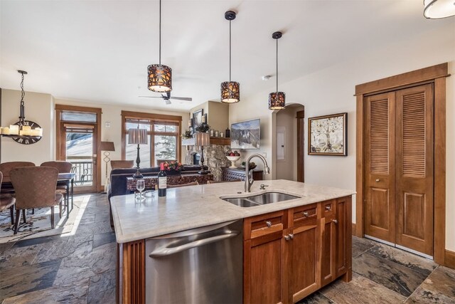 kitchen with stainless steel dishwasher, a sink, stone tile flooring, open floor plan, and a notable chandelier