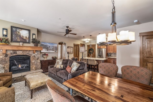 living area featuring arched walkways, a ceiling fan, a stone fireplace, and recessed lighting