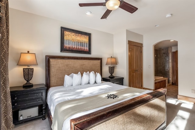 carpeted bedroom with ensuite bathroom, arched walkways, recessed lighting, and ceiling fan