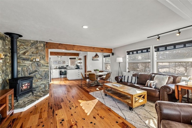 living room with light hardwood / wood-style floors, a wood stove, beam ceiling, and rail lighting