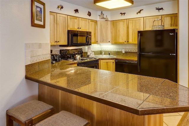 kitchen with a peninsula, a sink, backsplash, tile counters, and black appliances